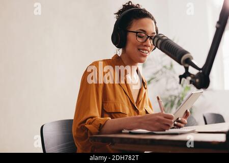 Junge Frau, die Podcast mit Mikrofon aufnimmt. Radio-Host, der von zu Hause aus arbeitet. Stockfoto