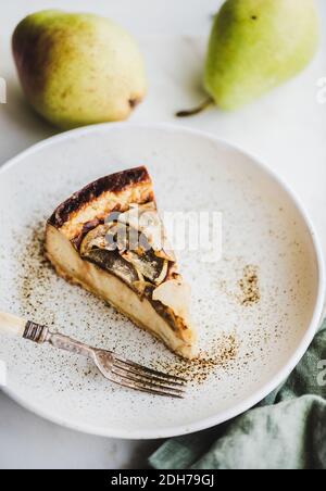 Stück vegan milchfrei zuckerfreier Birne Käsekuchen in rustikalem Teller über weißem Marmortisch Hintergrund, Draufsicht. Modernes vegetarisches gesundes Dessertkonzept Stockfoto