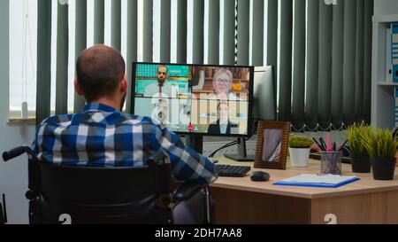 Behinderter Manager im Rollstuhl, der während der Videokonferenz im Geschäftsbüro online spricht. Gelähmt, immobilisiert Freiberufler arbeiten in Finanzunternehmen mit moderner Technologie. Stockfoto