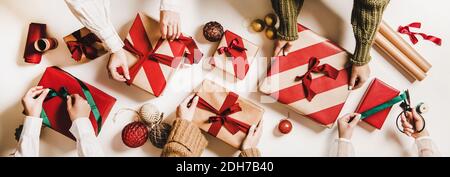 Flach-Lay von Völkern Hände Verpackung Geschenkboxen mit Geschenkpapier, bunte Kugeln, Kugeln, Bänder über schlichten weißen Hintergrund, Draufsicht. Weihnachten Urlaub trendy Grußkarte, Banner Stockfoto