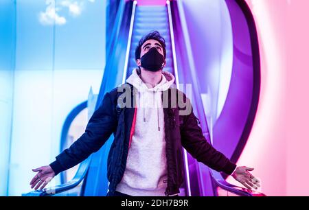Ein Schuss eines Mannes in einer medizinischen Maske stehend Auf einer Rolltreppe Stockfoto