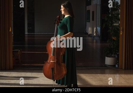 Teenager-Mädchen mit ihrem Cello, posiert in einem Flur. Stockfoto