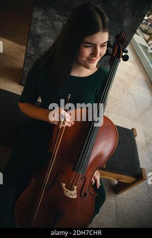 Teenager-Mädchen mit ihrem Cello, posiert in einem Flur. Stockfoto