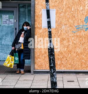 Kingston London, Dezember 09 2020, Junge Frau Trägt Schützende Gesichtsmaske Gespräch Auf Handy-Schutz In Shop Doorway Stockfoto