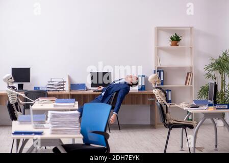 Junger männlicher Angestellter mit Skeletten im Büro Stockfoto