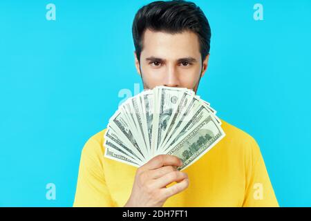 Glücklicher junger Mann hält Stapel Geld und prahlt mit seinem Einsparungen auf blauem Hintergrund Stockfoto