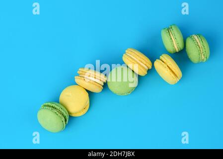 Gebackene gelbe und grüne Macarons Plätzchen liegen in einer Reihe Auf blauem Hintergrund Stockfoto