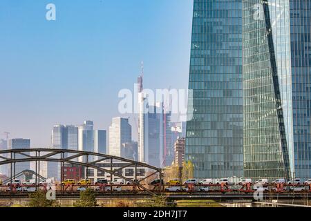 Güterzug mit vielen Autos über die Eisenbahnbrücke mit der Frankfurter Skyline im Hintergrund in Frankfurt am Main, Hessen, Deutschland. Stockfoto