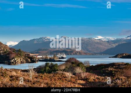 KYLE OF LOCHALSH ROSS-SHIRE SCHOTTLAND ZERKLÜFTETE KÜSTE MIT BOOTEN VOR ANKER AM UFER DES LOCH ALSH SCHNEIT ES AUF DEN HÜGELN Stockfoto