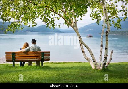 Ein Paar mittleren Alters sitzt auf einer Bank mit Blick über einen See in Whitefish, Montana, USA Stockfoto