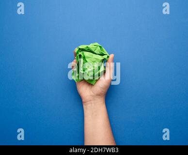 Weibliche Hand hält zerknitterte Kugel aus grünem Papier auf blau Hintergrund Stockfoto