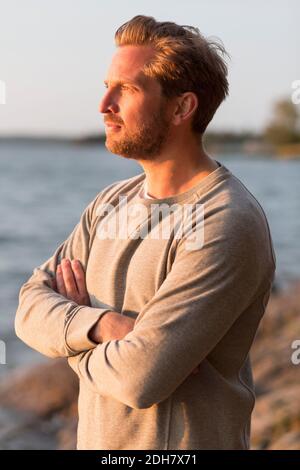 Nachdenklicher Mann, der Arme am Strand kreuzt Stockfoto