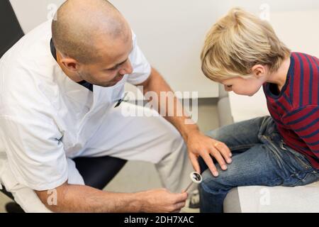 Männlicher Orthopäde überprüft Kniereflexe des Jungen in der Klinik Stockfoto