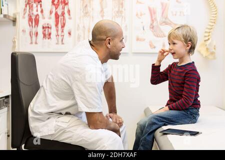 Männlich orthopädischen Arzt im Gespräch mit Jungen auf Untersuchungstisch sitzen In der Klinik Stockfoto