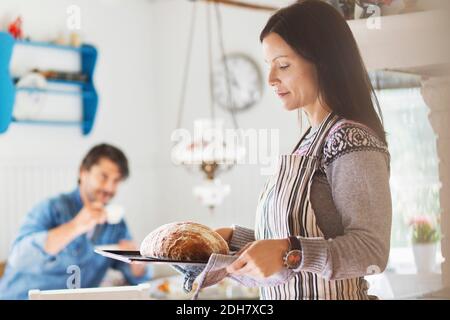 Frau hält frisch gebackenes Brot im Tablett mit Mann in Hintergrund zu Hause Stockfoto