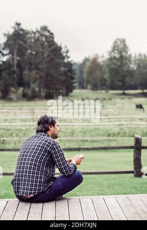 Rückansicht des männlichen Bauern auf der Veranda sitzen bei Bio Bauernhof Stockfoto