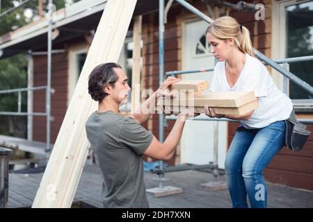 Seitenansicht eines Paares, das einen Holzstapel vor dem Haus trägt Wird gerade renoviert Stockfoto