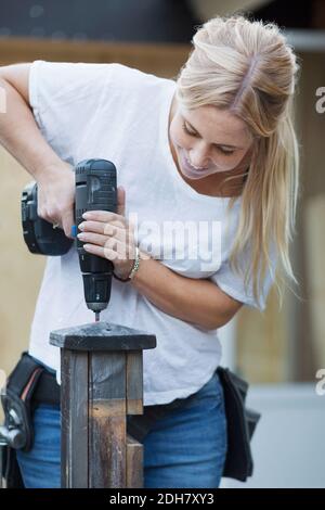 Glückliche Frau mit Akku-Schraubendreher auf Holzpfosten Stockfoto