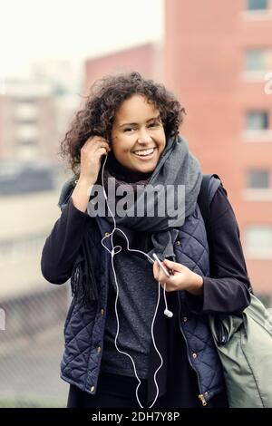 Portrait einer glücklichen Universitätsstudentin in warmer Kleidung Kopfhörer im Freien Stockfoto