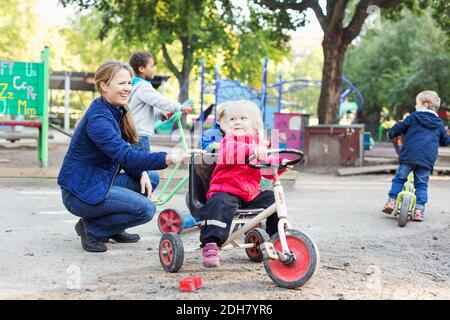 Glücklich weibliche Lehrer Mädchen zu helfen, Dreirad auf Spielplatz zu fahren Stockfoto