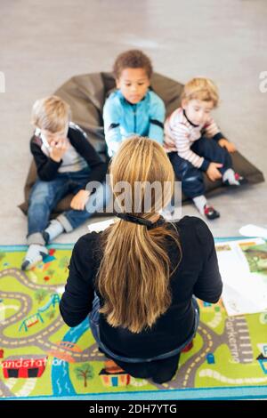 Hochwinkelansicht des Lehrers, der vor Kindern sitzt Im Kindergarten Stockfoto