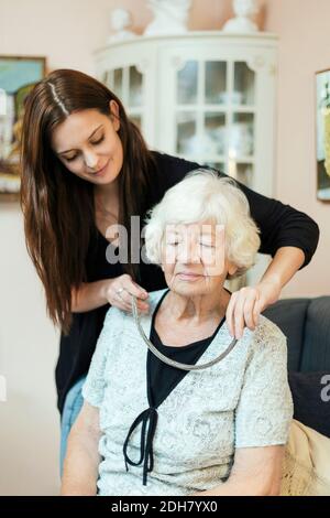 Enkelin, die Halskette an Großmutter zu Hause aufsetzt Stockfoto