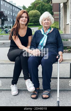 Portrait einer lächelnden Frau, die mit Enkelin auf der Bank im Freien sitzt Stockfoto