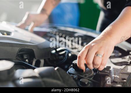 Zugeschnittenes Bild einer Mechanikerin, die Kühlmittel im Auto öffnet Stockfoto