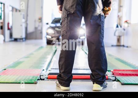 Niedriger Abschnitt des Mechanikers, der vor dem Auto steht, das kommt In Richtung Hydraulikhub Stockfoto