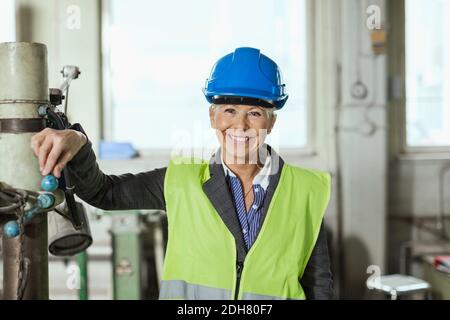 Portrait einer glücklichen reifen Arbeiterin, die in der Fabrik einen Hardhut trägt Stockfoto