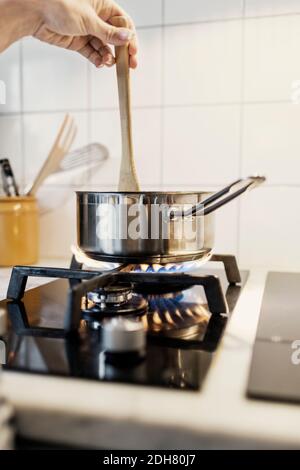 Zugeschnittenes Bild der Frau Hand hält Spatel in Soße Pfanne Beim Kochen von Speisen auf dem Herd Stockfoto