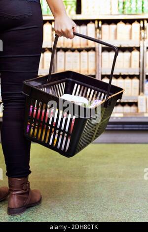 Niedriger Abschnitt der Frau, die Korb im Supermarkt trägt Stockfoto