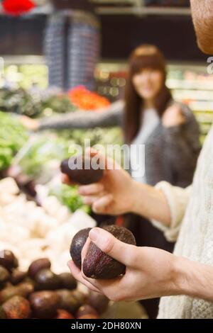 Mittelteil des Mannes hält Avocados im Supermarkt mit Frau in Hintergrund Stockfoto