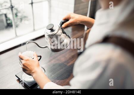 Zugeschnittenes Bild einer Barista, die kochendes Wasser in den Kaffee gießt Filter im Café Stockfoto