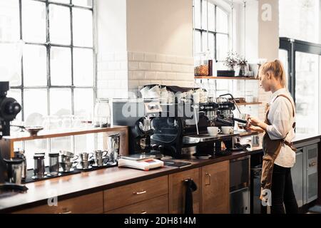 Weibliche Barista, die die Kaffeemaschine im Café benutzt Stockfoto