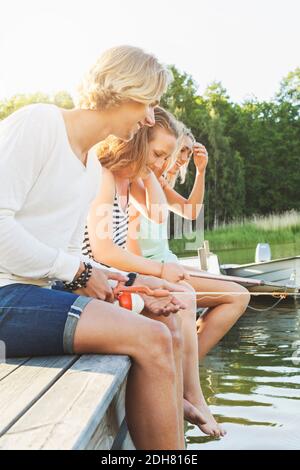 Glückliche Freunde beim Angeln, während sie auf dem Pier am See sitzen Stockfoto