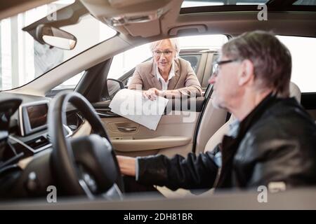 Leitende Verkäuferin erklärt dem im Auto sitzenden Mann die Merkmale Kaufen Stockfoto