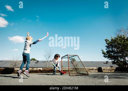 Aufgeregt Mädchen spielen Hockey mit Jungen im Hof gegen blau Himmel Stockfoto