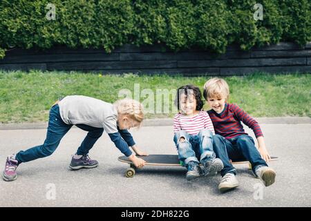 Mädchen schiebt Freunde sitzen auf Skateboard auf Hof Stockfoto