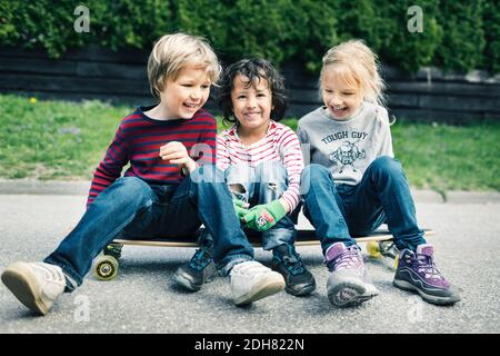 Spielerische Freunde sitzen auf dem Skateboard auf dem Hof Stockfoto