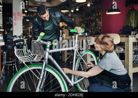 Weibliche Mechanikerin, die Fahrrad analysiert, während sie mit dem Kunden in der Reparatur spricht Kaufen Stockfoto