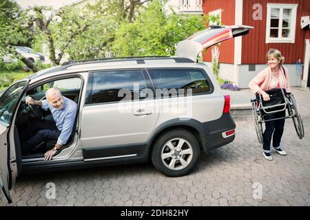 Behinderter Mann im Auto, der die Frau ansieht, die den Rollstuhl trägt Straße Stockfoto