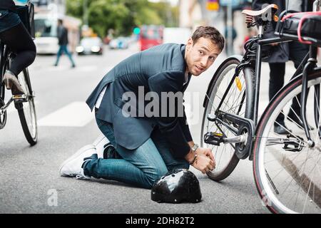 Geschäftsmann schaut weg, während Reparatur Fahrrad auf der Straße Stockfoto