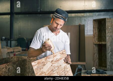 Zimmermann, der den Leim auf die hölzerne Planke in der Werkstatt anwendet Stockfoto