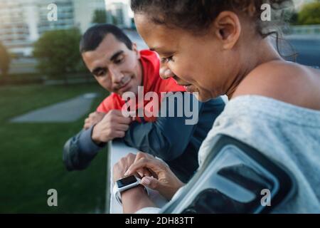 Mann, der einen Freund mit einer intelligenten Uhr ansieht, während er dabei steht Geländer auf dem Bürgersteig Stockfoto