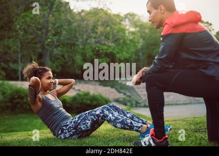 Mann kniet und schaut auf Frau Sit-ups auf dem Feld Stockfoto