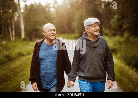 Glückliches schwules Paar, das weg schaut, während es auf der Straße mitten geht Bäume Stockfoto