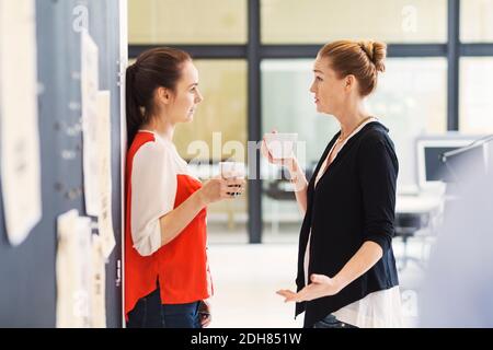 Seitenansicht der Geschäftsfrauen diskutieren beim Kaffee im Büro Stockfoto