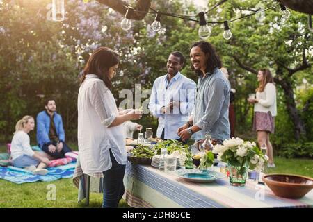 Multiethnische Freunde, die am Esstisch im Hinterhof Essen zubereiten Stockfoto