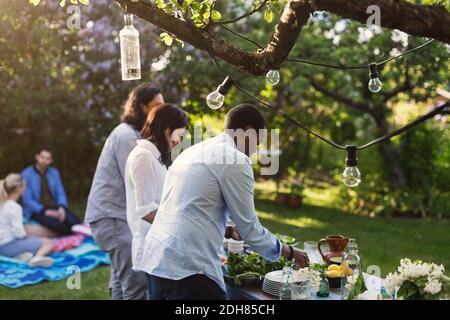 Freunde, die während der Sommerparty am Tisch im Hof Essen zubereiten Stockfoto